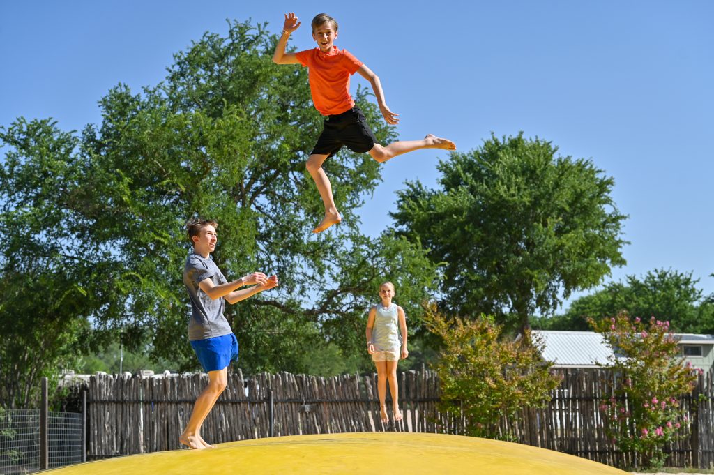 Three kids bouncing on yellow trampoline outdoors at a Jellystone Park Camp-Resort.