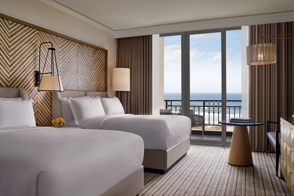 Deluxe guestroom with two queen beds, fresh white sheets and an oceanview through the balcony windows of the Ritz Carlton Amelia Island resort.