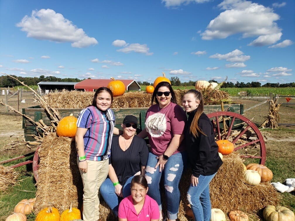 Family leaning on a wago full of hay bales poses for a photo surrounded by pumpkins. c. Hubbs Farm, North Carolina