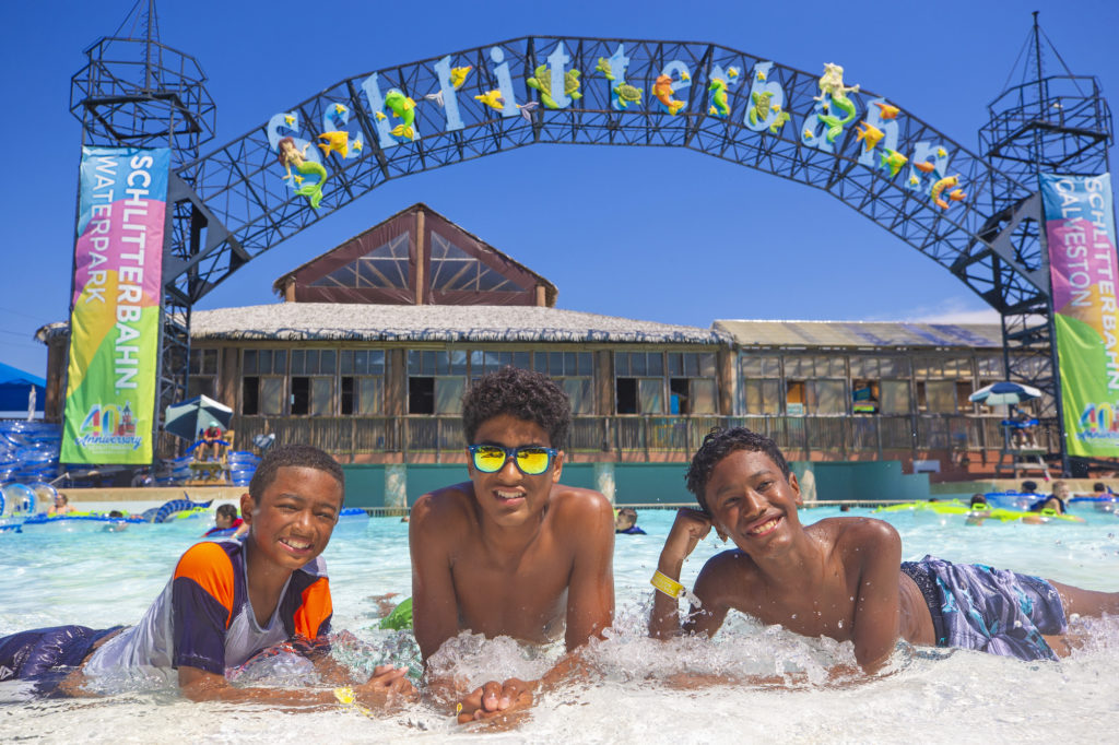 Three boys in a pool get their picture taken in front of the Schlitterbahn Galveston sign.