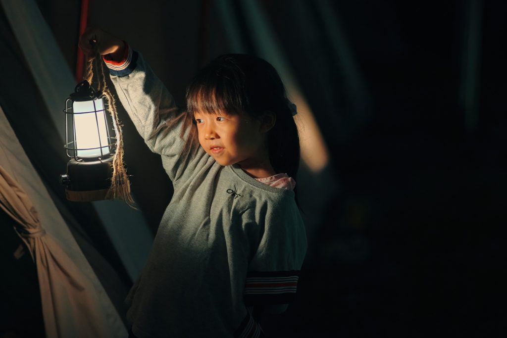 Girl holidng kerosene lantern in a tent at night.