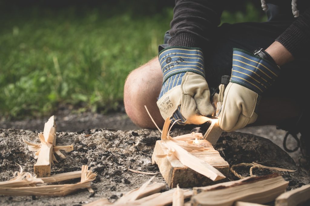 Hands in work gloves handle wood chips to make kindling for a campfire.