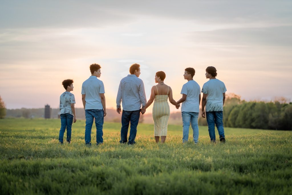 Mixed family of adults and kids watch sunset in a field.