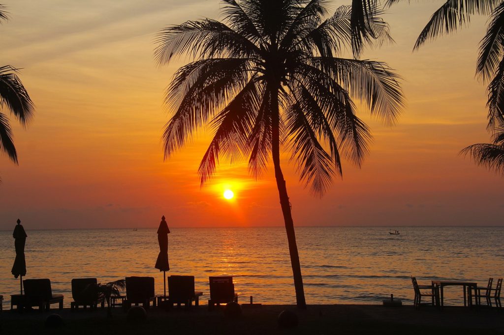 Sunset over the Andaman Sea in Thailand with beach chairs in the foreground.