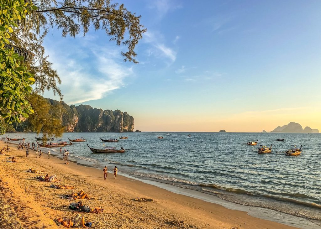 Gold sand beach with people sunbathing and fishing boats off the coast of Thailand.