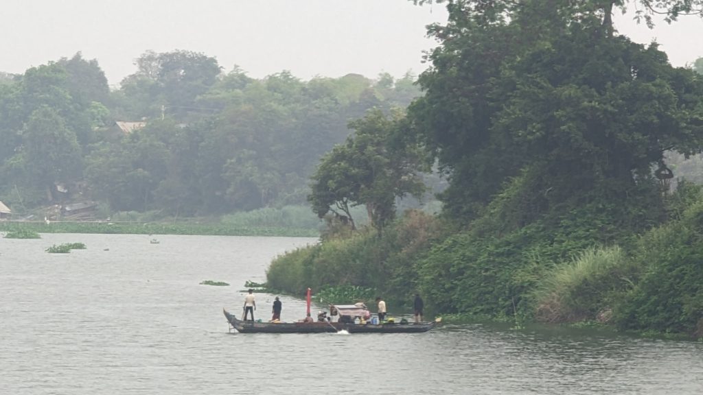 A fishing boat with family aboard leaves the Mekong River shoreline to fish with nets at dawn.