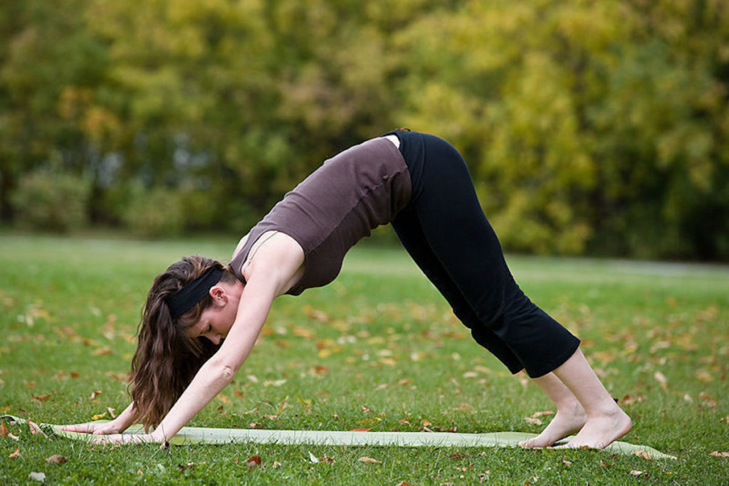 Girl doing downward facing do yoga position on a mat outdoors.