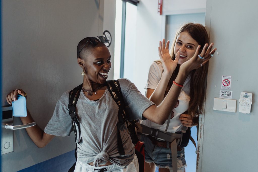 Two women laughing as they enter hotel room with key card.