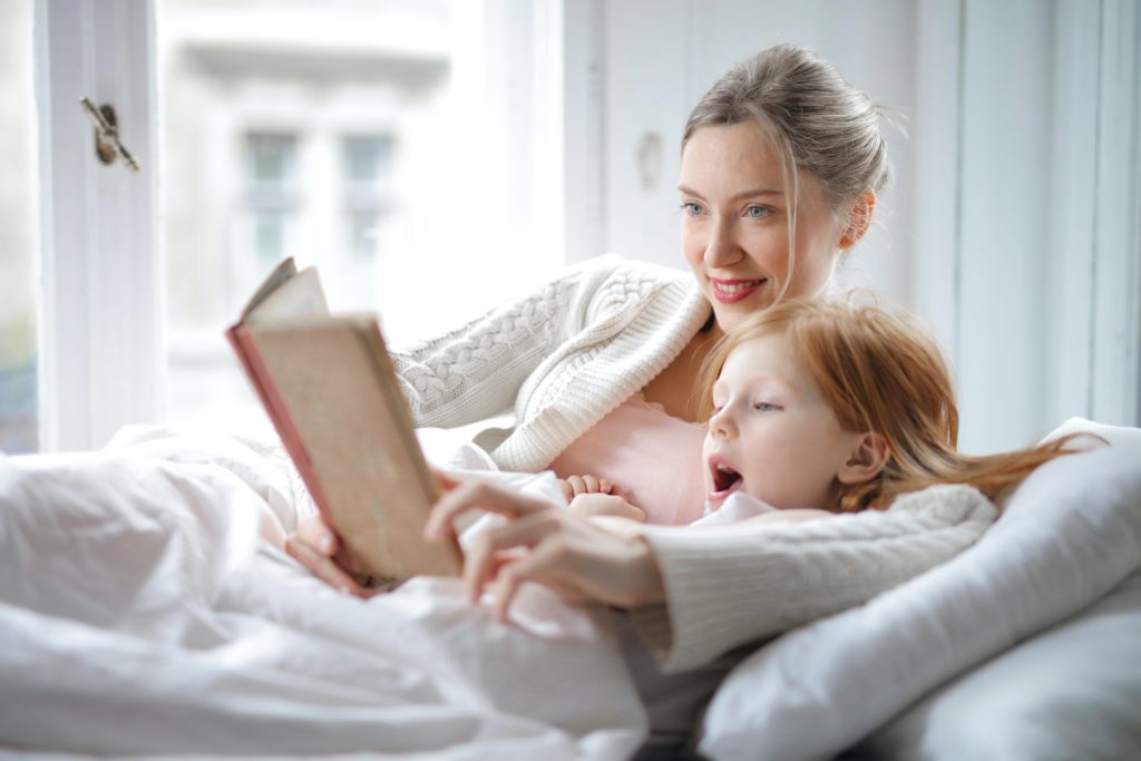 Mom and daughter reading a book in bed together.