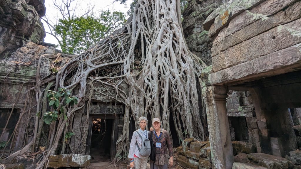 Couple pose in front of ancient Banyan tree at the Ta Prohm temple seen in 
