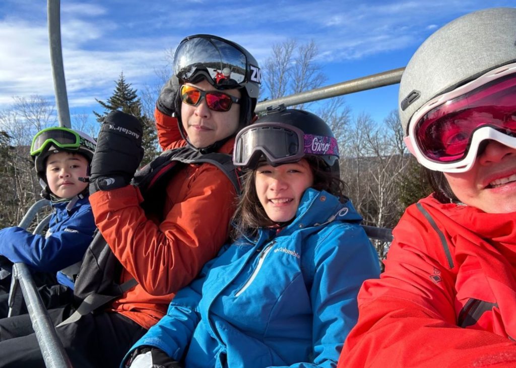 Family of four in ski helmets on a chairlife in Maine.