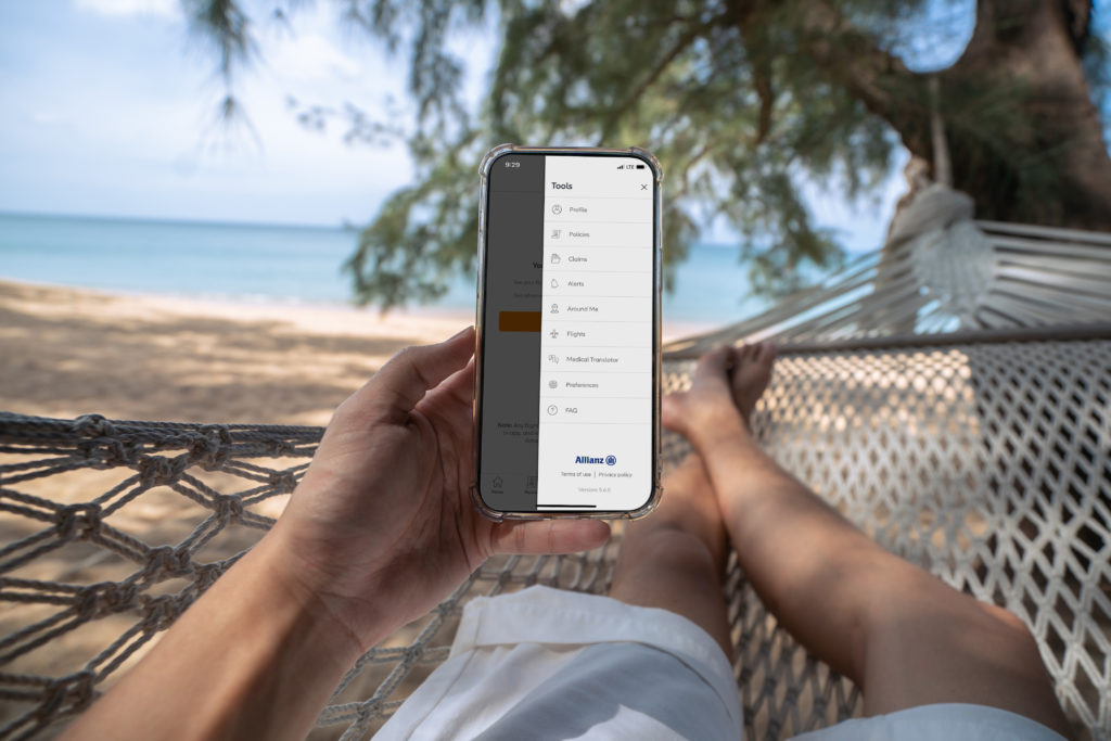 Woman in a hammock looks at the Allianz Travel Insurance TravelSmart app while relaxing at the beach. Photo c. Allianz Travel USA