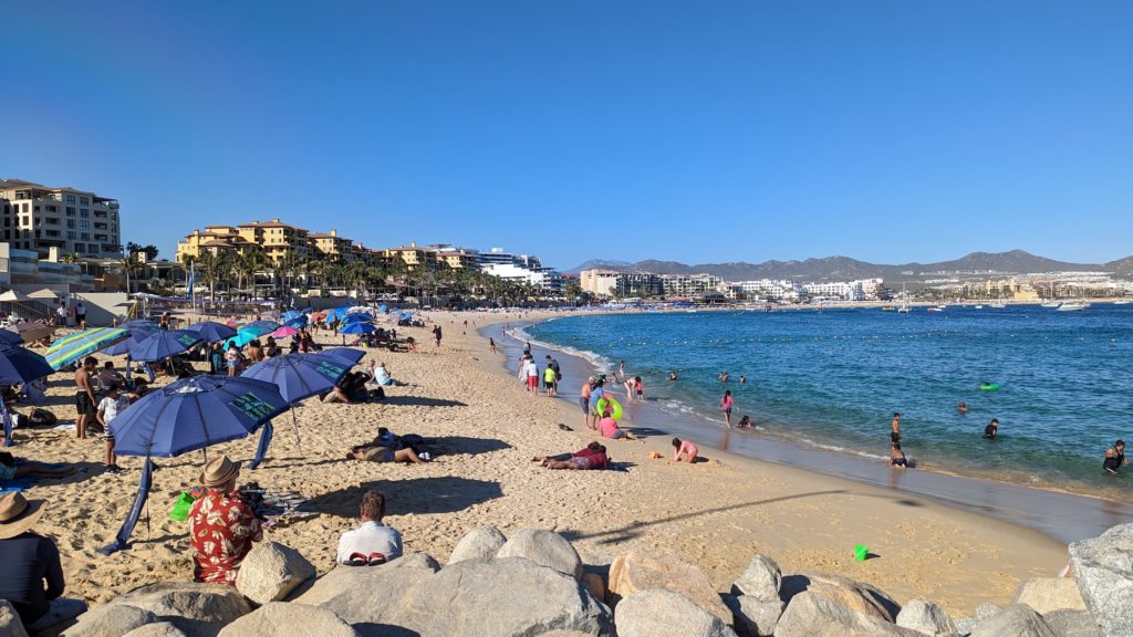 Crowds play and sunbathe on the busy public beach lined with the top Los Cabos resorts in Cabo San Lucas, Baja Calfornia Sur, Mexico.