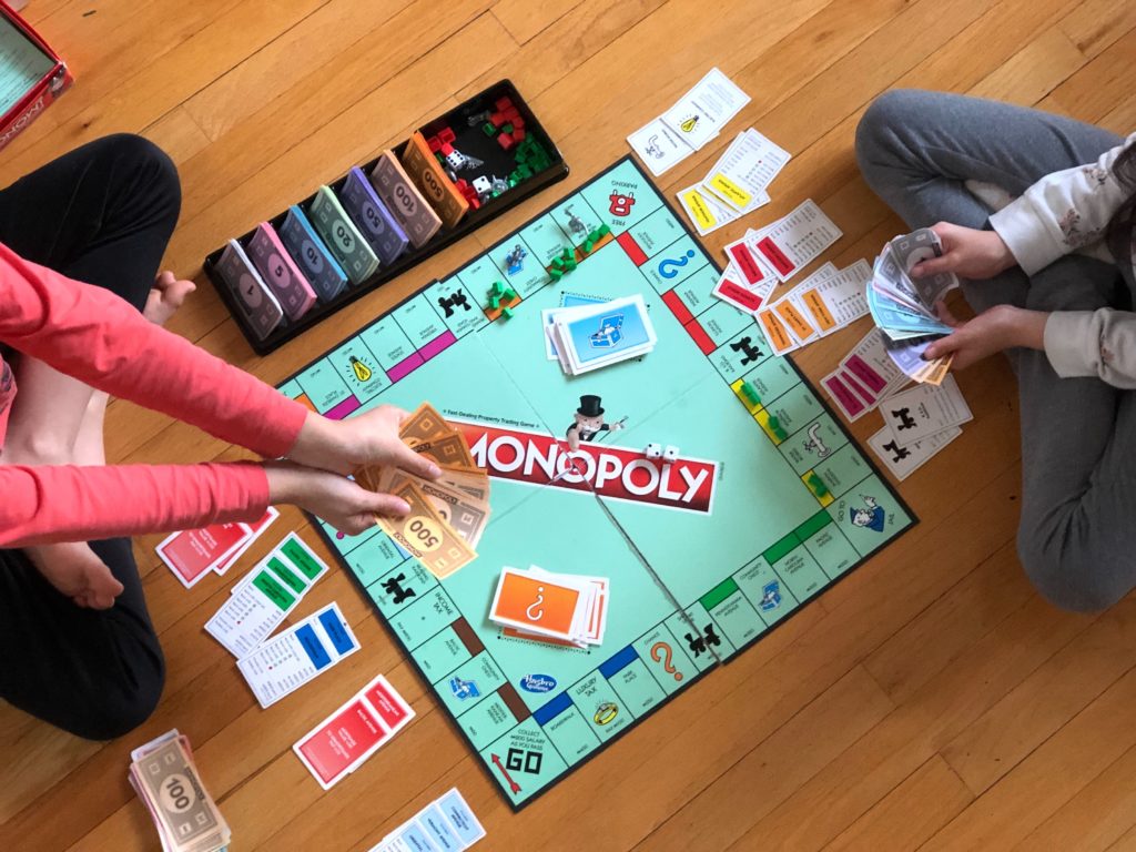 Two people playing Monopoly board game on the floor.