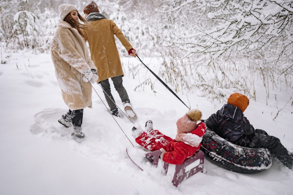 Mom and Dad pulling 2 small children through the snow on their own sleds.