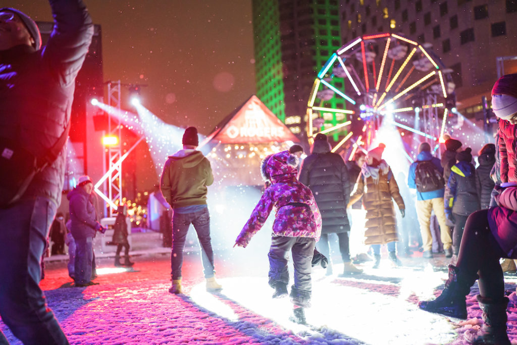 Families watch live outdoor show in the snow at the Montreal en Lumiere Festival, a top family getaway in Canada. Photo c. Benoit Rousseau for 2023 Montreal en Lumiere Festival.