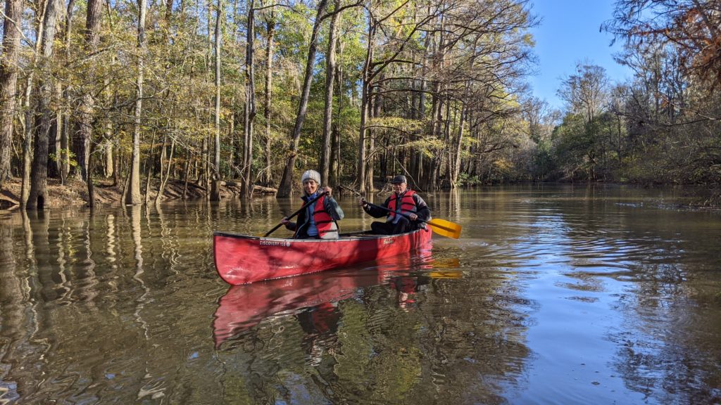 Two rowers in a red canoe paddle through the swamps at Congaree National Park in South Carolina.