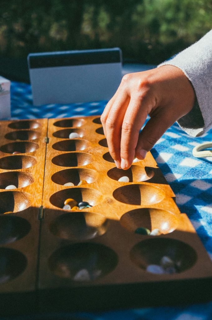 Man's hand holds wooden board for the game mancala. Photo c. Tobias Tullius for unsplash.