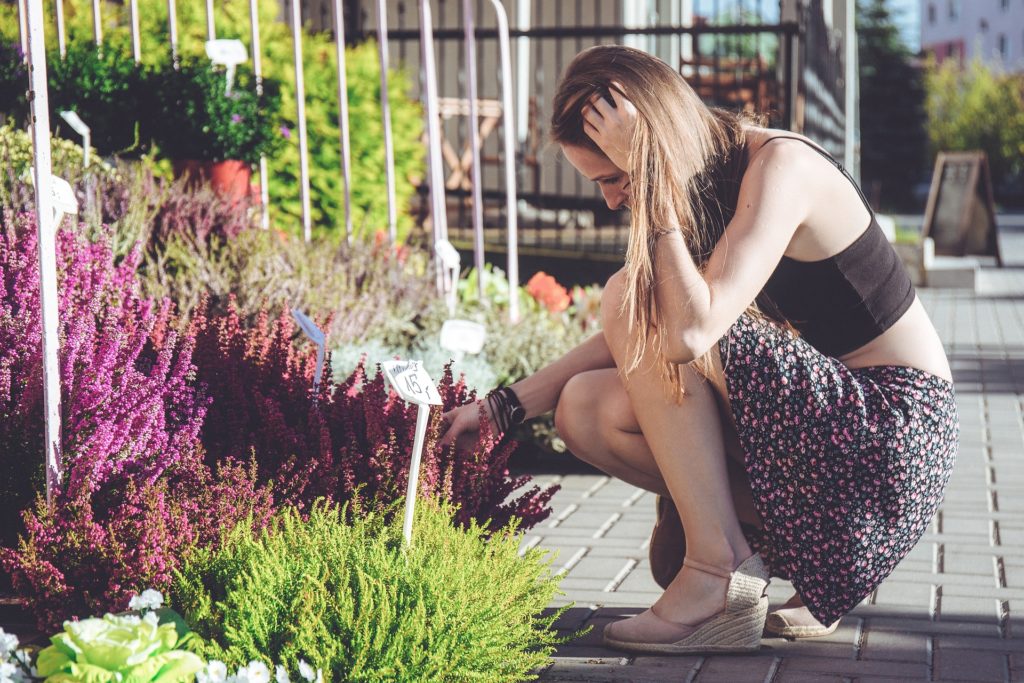 Woman kneels by the plants and herbs at a green market in a city. photo c. pixabay.