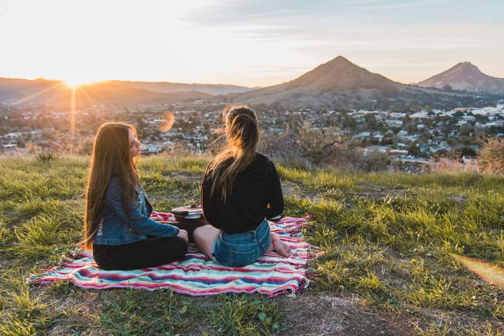 Two women have picnic on grass field in site of mountains in San Luis Obispo, California. Photo c. Luke Bender for unsplash