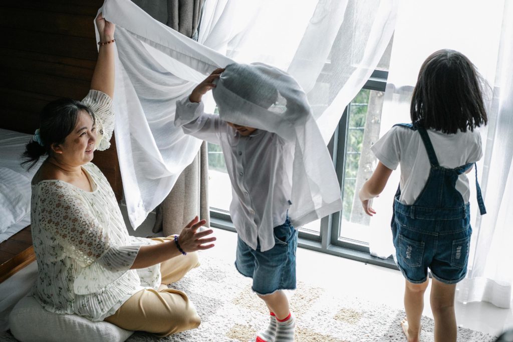 Asian grandma who babysites on the road has girl and boy wrapping themselves in sheer white curtains. Photo by Alex Green for pexels.