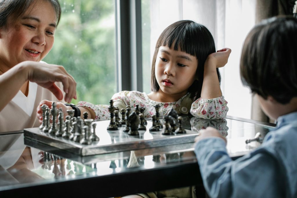 Asian nanny plays chess with two kids in front of a window. Photo by Alex Green for pexels.com