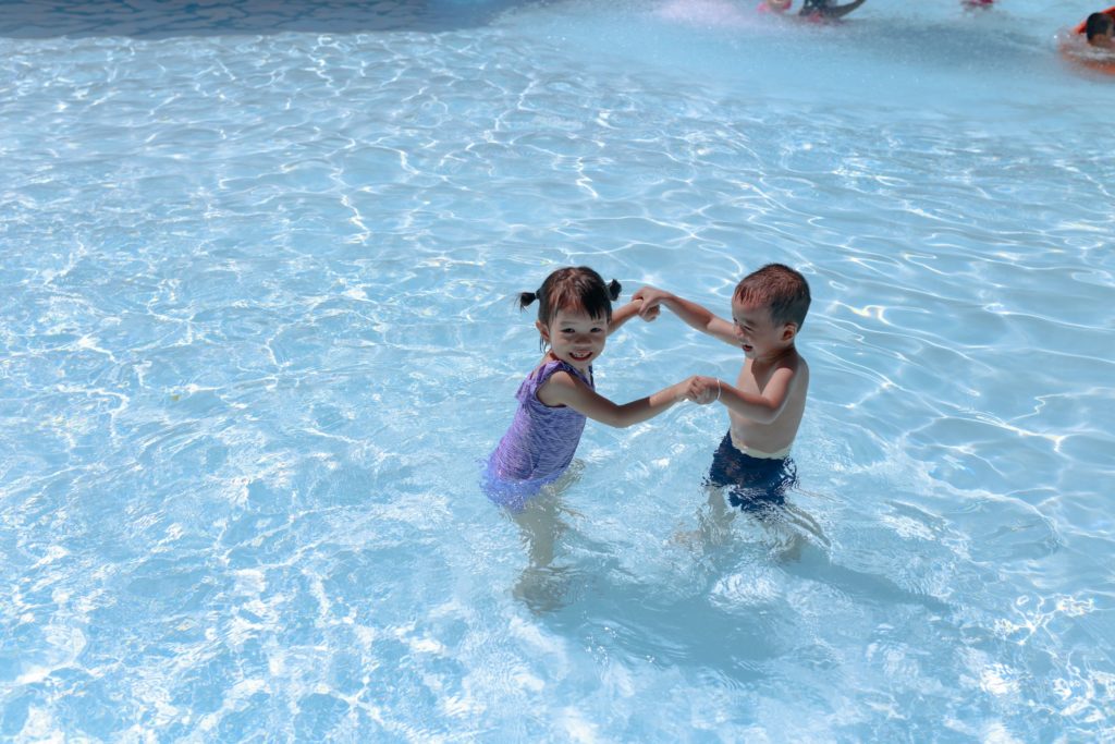 Little girl and boy holding hands while standing in a swimming pool.