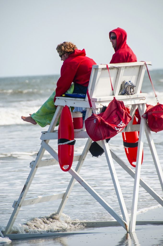 Two lifeguards at the beach in red hoodies and sunglasses are protected from the sun.