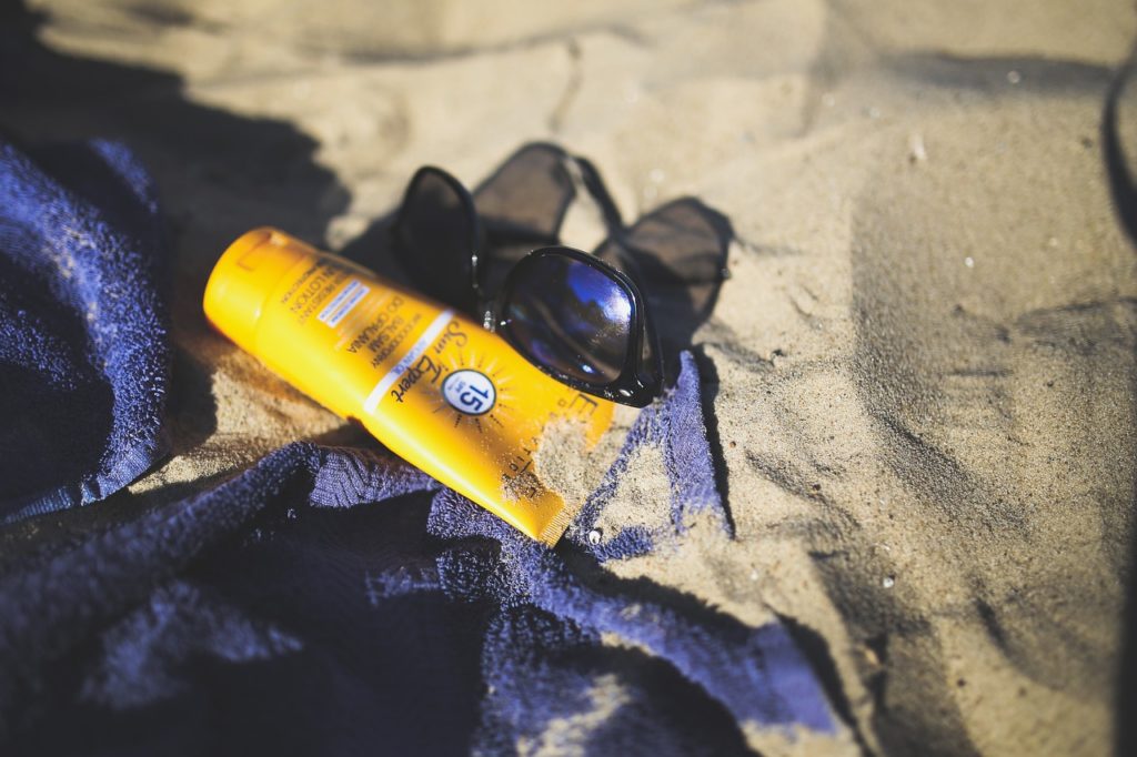 Beach towel with SPF 15 sunblock tube and sunglasses surrounded by sand.