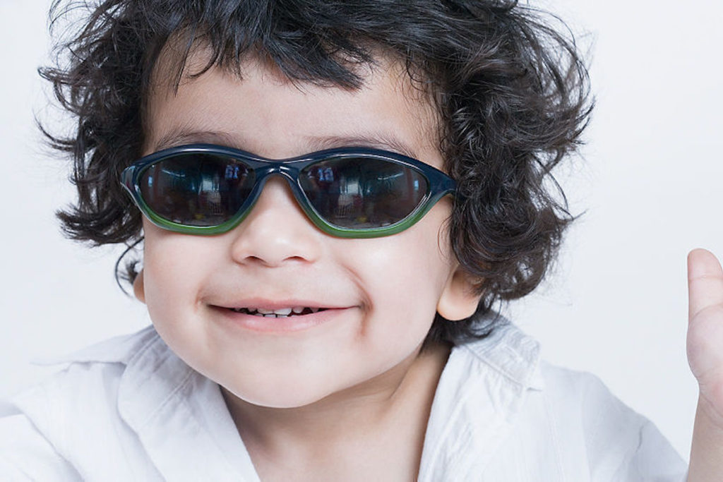 Criança sorridente aprendendo a nadar usa óculos escuros e roupão de praia.