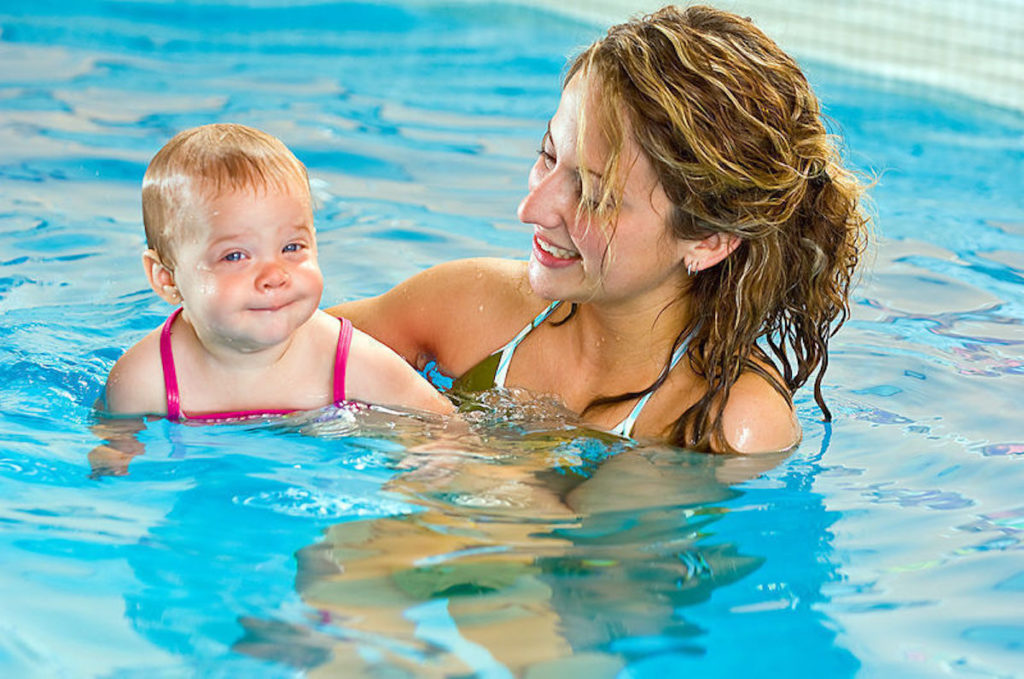 Mulher ensina bebê a nadar na piscina coberta.