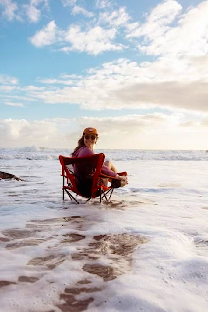 Woman sitting on an REI Skyward Campchair in the surf at the beach. Photo c. REI.com