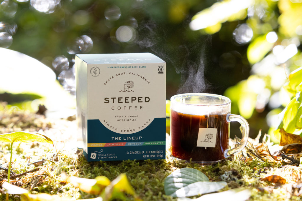 Box of Steeped Coffee and a cup of brewing coffee shown outdoors on a lawn. Photo c. Steeped Coffee