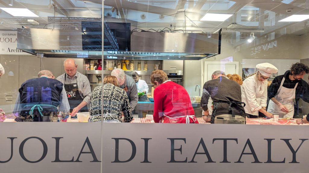 Group of tourists working with chefs at the cooking school at Eataly, the food hall to visit with one day in Milan, Italy.
