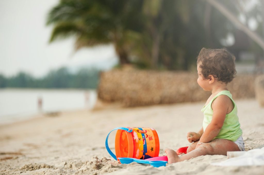 Bebê brincando com balde na areia em uma praia na Espanha.