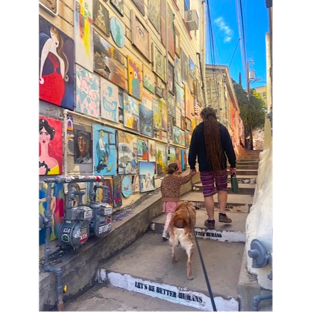 Author, daughter and dog walk past paintings and a "Let's Be Better Humans" step on Bisbee's 1,000 Step Staircase. Photo by Victor Aziz.