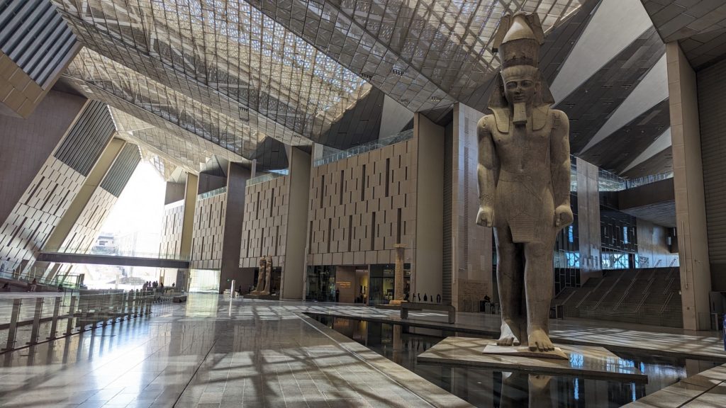 A monumental limestone statue of Pharaoh Ramsses II greets visitors in the Grand Hall of the Grand Egyptian Museum.