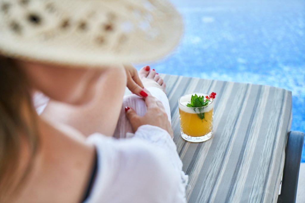 Woman enjoying a cocktail by the pool while sitting on a chaise lounge. Photo by Engin Aykurt for pixabay
