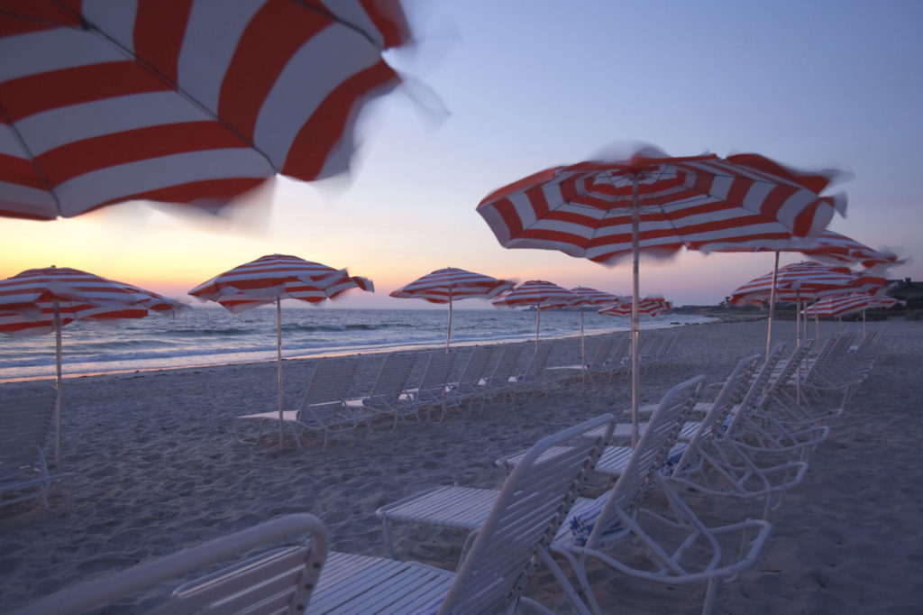 Striped beach umbrellas flap in the breeze at dusk outside a family hotel on the famous Cape Cod beach.