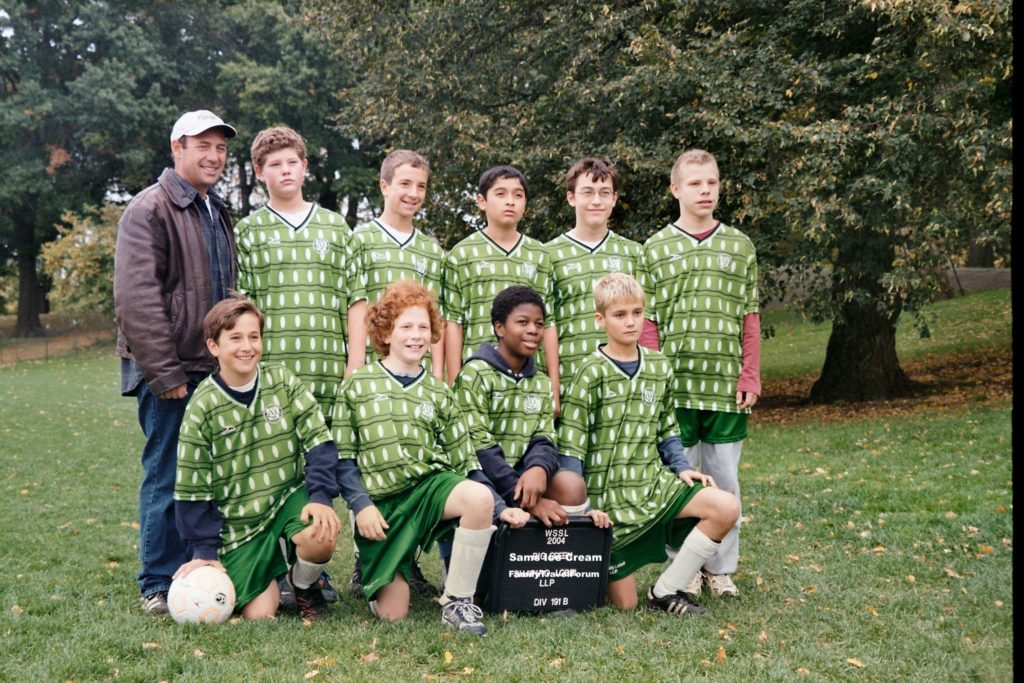 Boys soccer team poses with coach in a park.