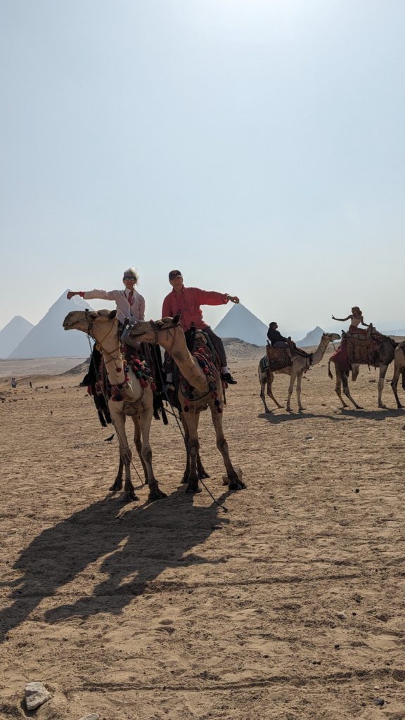 Tourists on camels appear to touch the tips of the Pyramids of Giza.