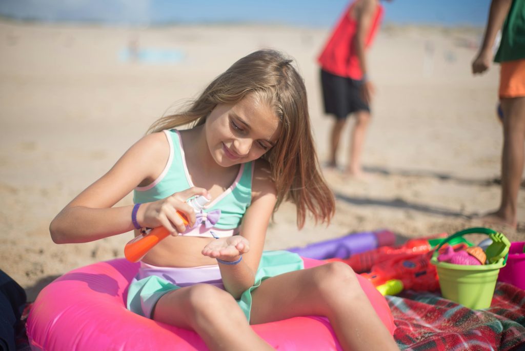 Girl sitting on float on the sand squirts sunblock from a bottle. Photo c. campus for pixels.