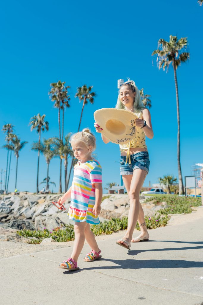 Mom follows daughter trying to put straw hat on her head at the beach. Photo c. kindelmedia for pixels.