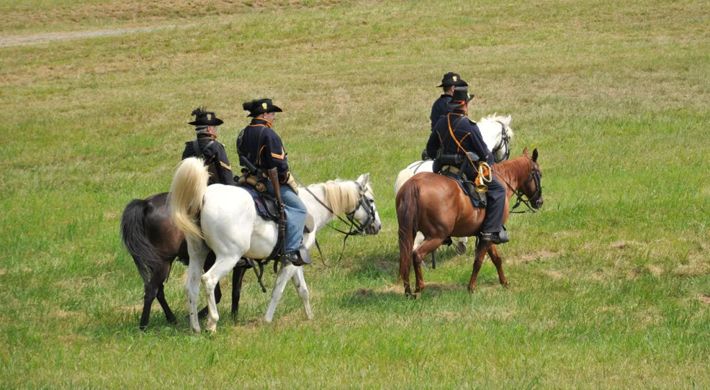 Uniformed living history reenactors on horseback ride across the battlefield at Gettysburg National Park. Photo c. NPS