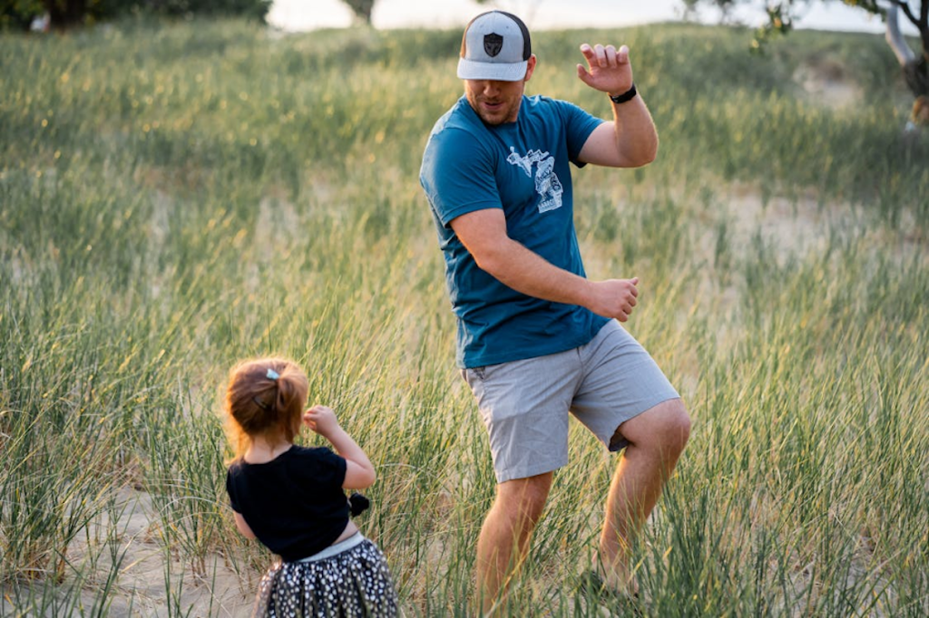 Man and girl playing in the grass near a beach.