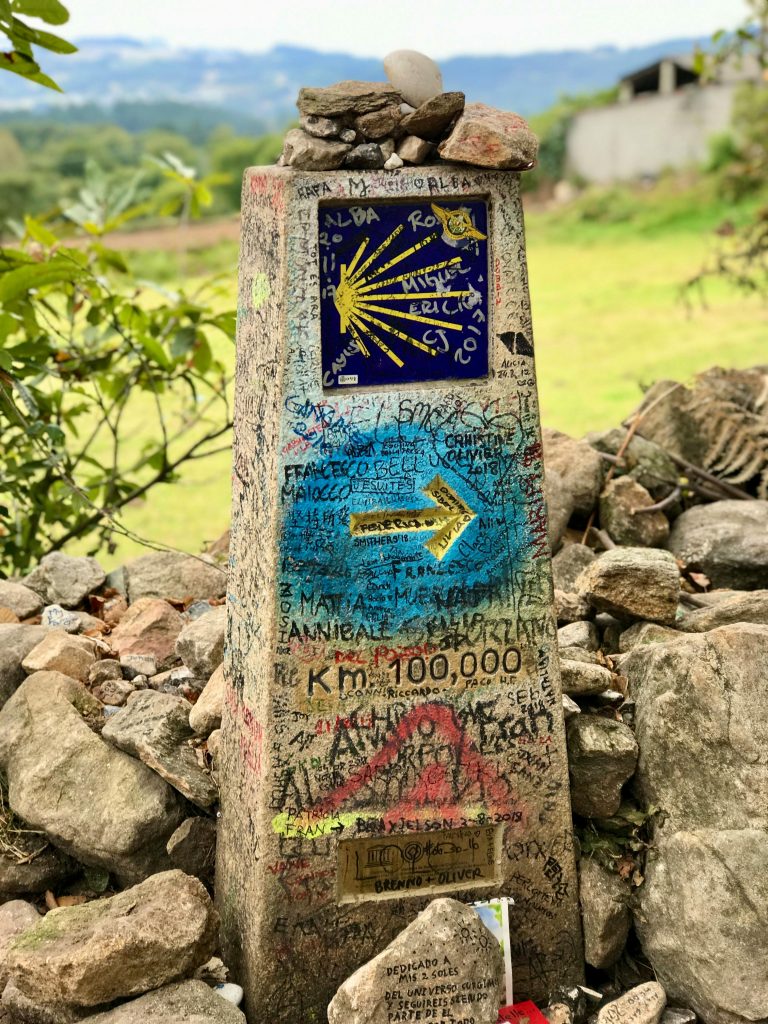 A stone trail marker is covered in graffiti and the signatures of passersby on the Camino de Santiago. Photo by Luis Andrade for pexels