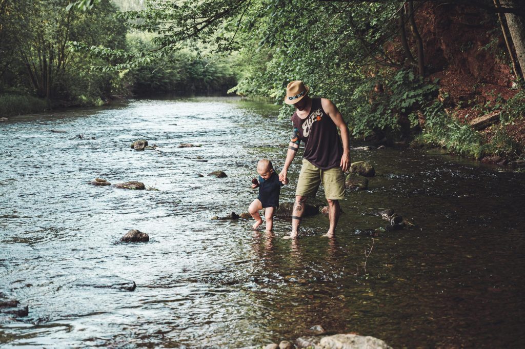 Father and child play in shallow river and cool their feet off in the water. Photo by Jan Koprivakart for pexels