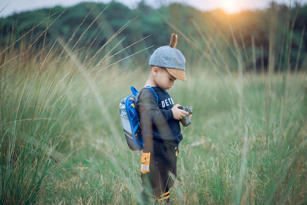 Young boy uses camera in his hands to take a picture of the grass in front of him. Photo c. soldiervip for pixels.