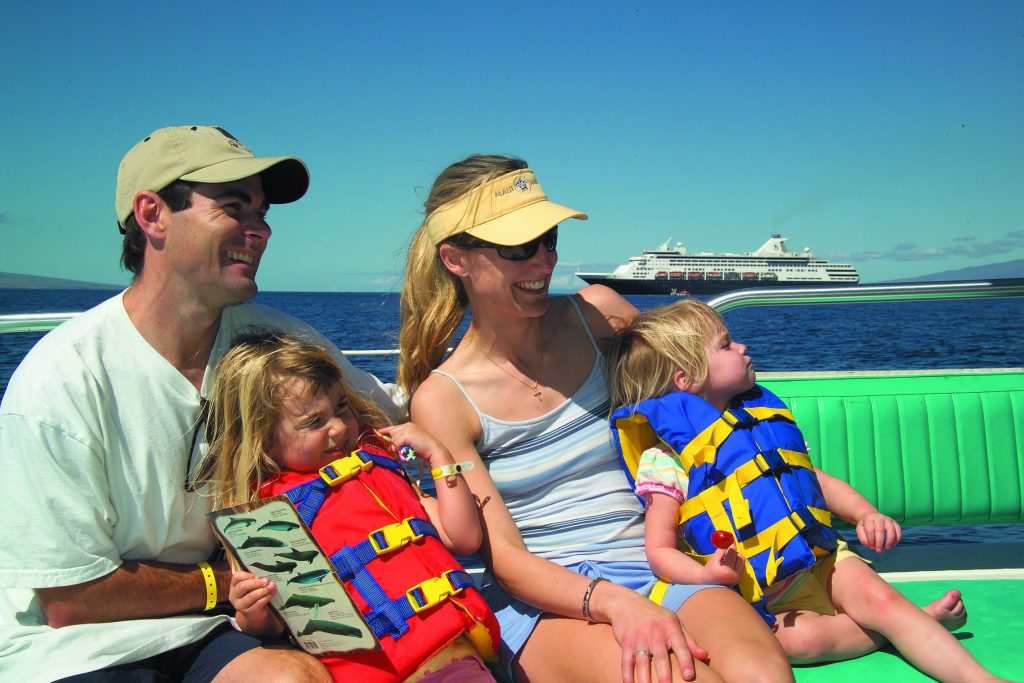 Parents holding girls in life jackets on a boat.