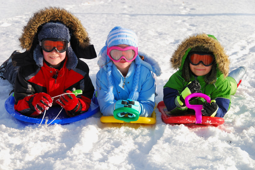 three kids with sleds in the snow on a spring break ski trip.